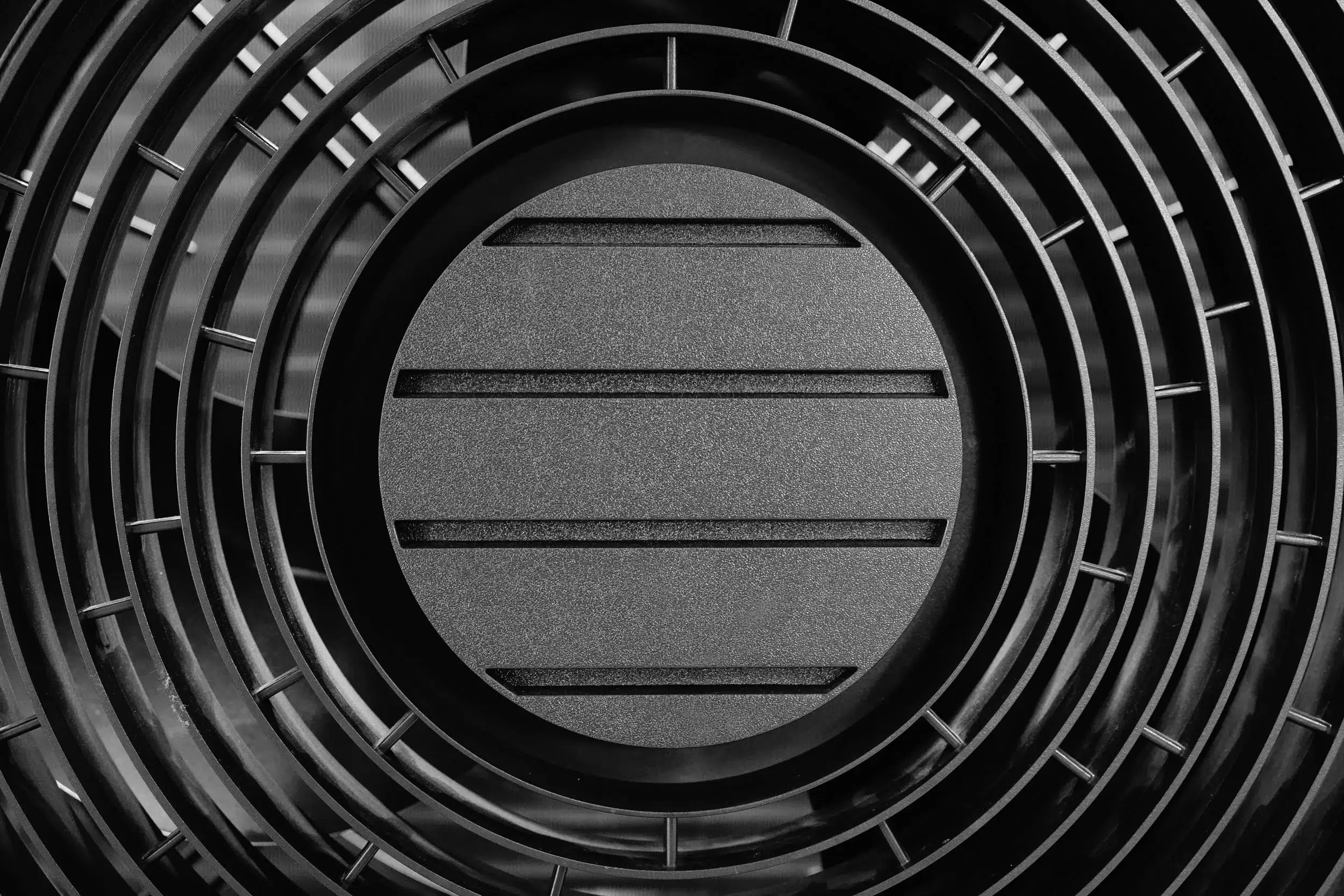 Nahaufnahme von konzentrischen, kreisförmigen Metallringen, die eine massive zentrale Scheibe umgeben und ein geometrisches, abstraktes Muster in Graustufen bilden.