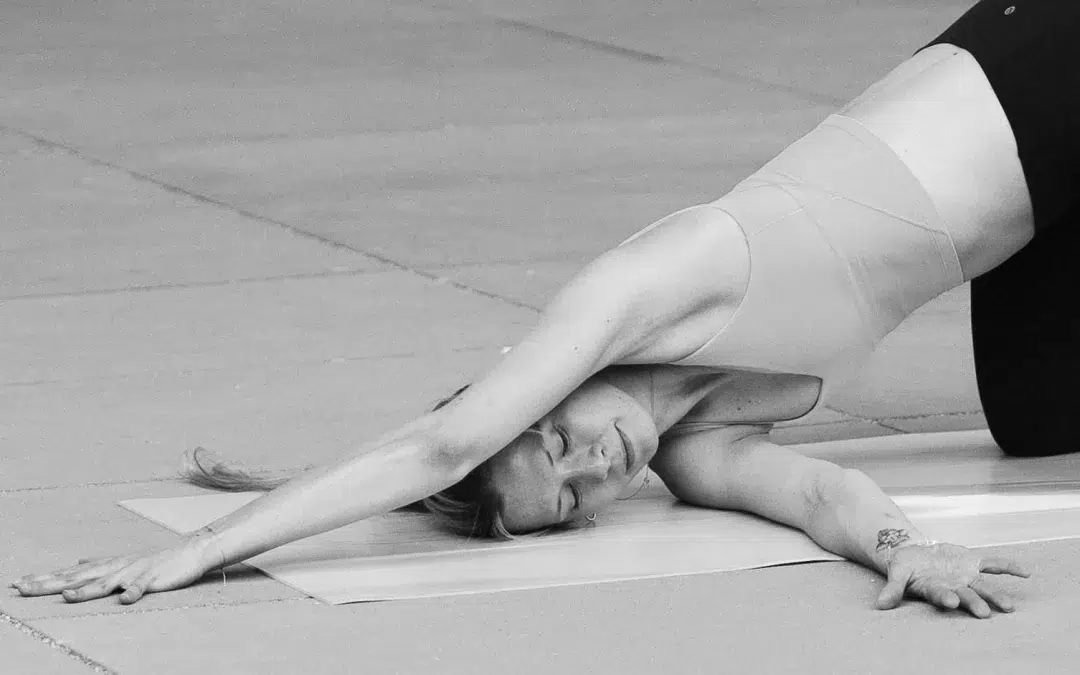 Eine Person auf einer Yogamatte streckt einen Arm nach vorne und legt den Kopf auf die Matte, während sie eine Yoga-Übung ausführt. Das Bild ist in Schwarz-Weiß gehalten.