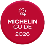 Logo des Michelin-Führers 2026 mit einem stilisierten, blumenförmigen Schlüssel auf rotem, rundem Hintergrund.